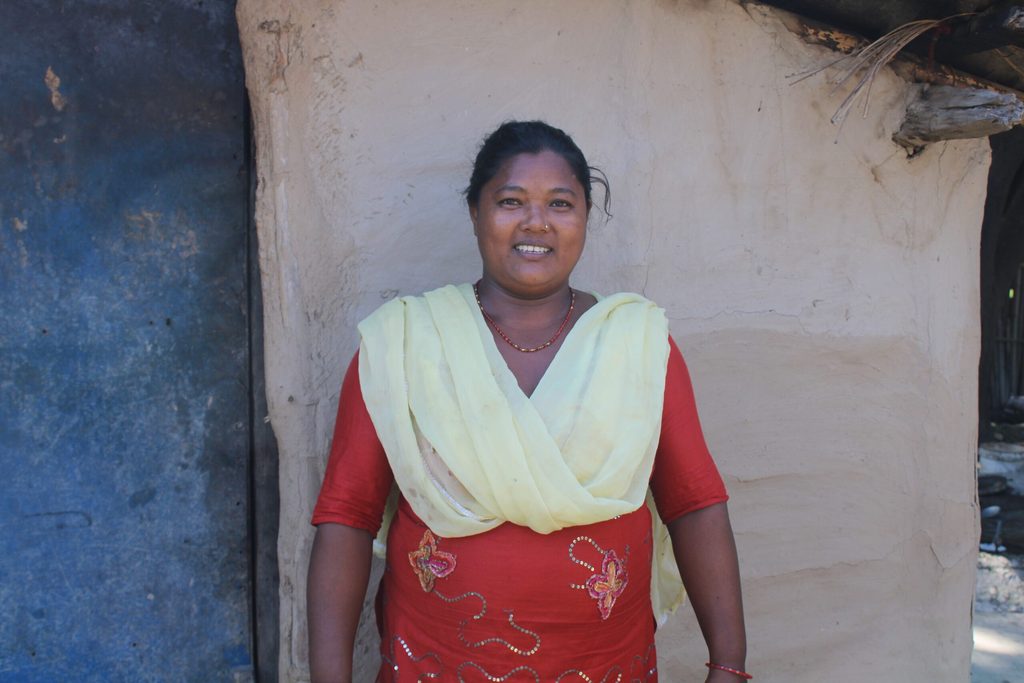 Gulfi wearing a red dress and yellow shawl in front of her home.