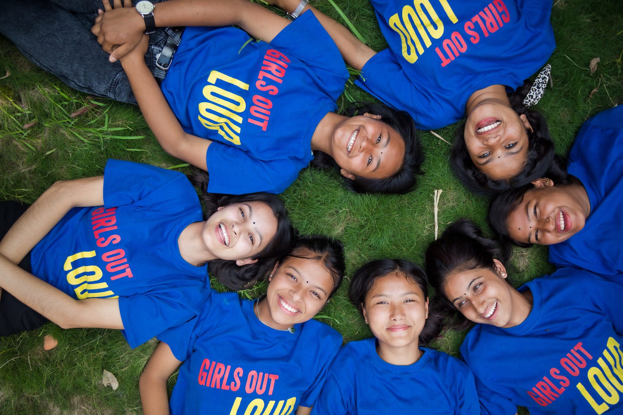 Members of the Girls Out Loud group in Nepal lay on the grass in a circle, smiling.