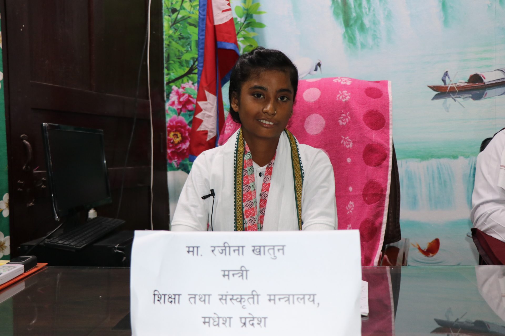 Rajina smiling and posing with her name as Minister of Education and Culture. 