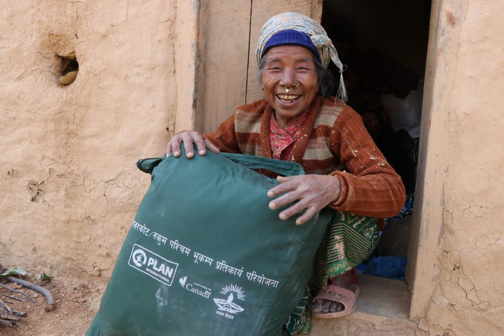 Birvi sitting in front of her house and showing the winterisation kit.
