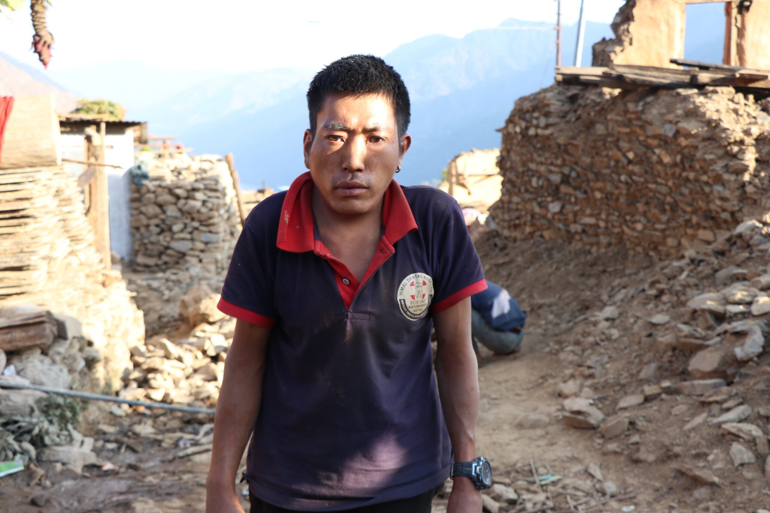 Dekbir standing in front of a village damaged by recent earthquake in Jajarkot. 