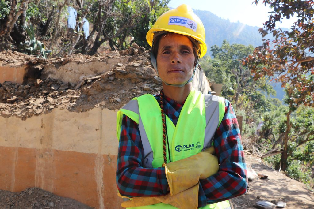 Deukali wears her hard hat and reflective jacket and stands with her arms folded.