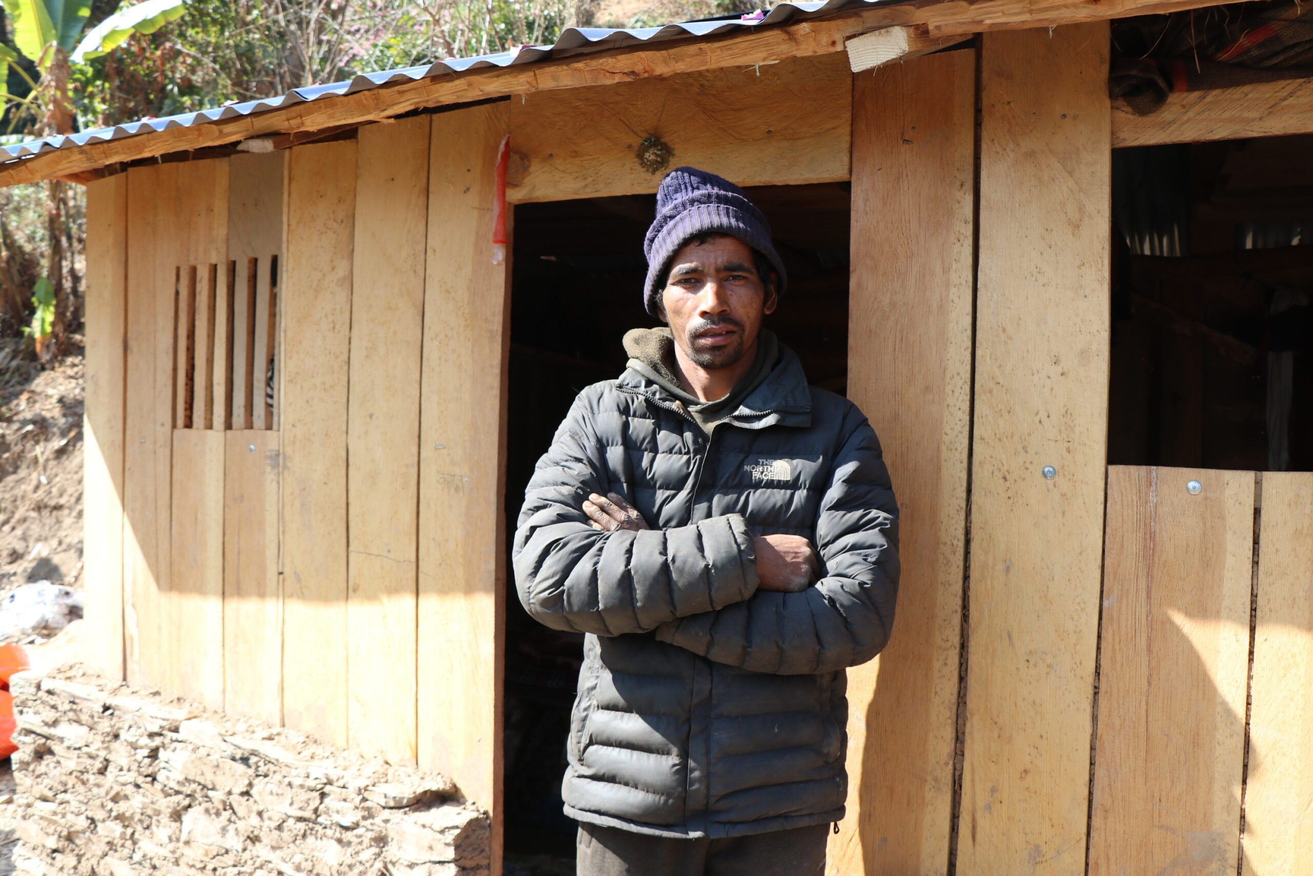 A man standing in front of his transitional shelter and folding his arms. 