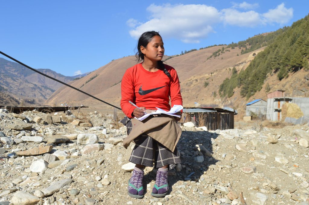 Young girl wearing orange tshirt holding notebook and pen.