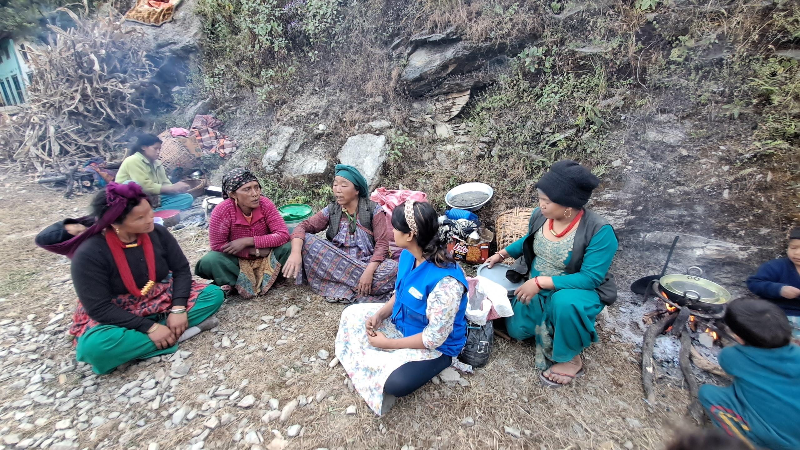 Plan's staff with women sitting on the floor and cooking in open sky after earthquake.