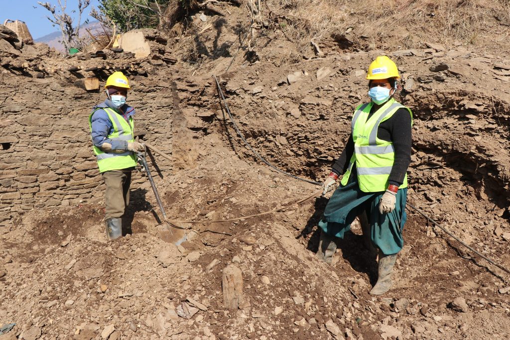 Parbir and a Deepa wearing yellow vest, hard hat and carrying shovel and clearing debris at their home.