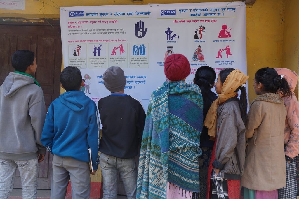 Eight people are looking into the poster related to protection messages during relief distribution.