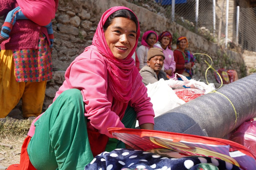 A woman wearing pink shawl on her head and pink jacket receiving NFIs.