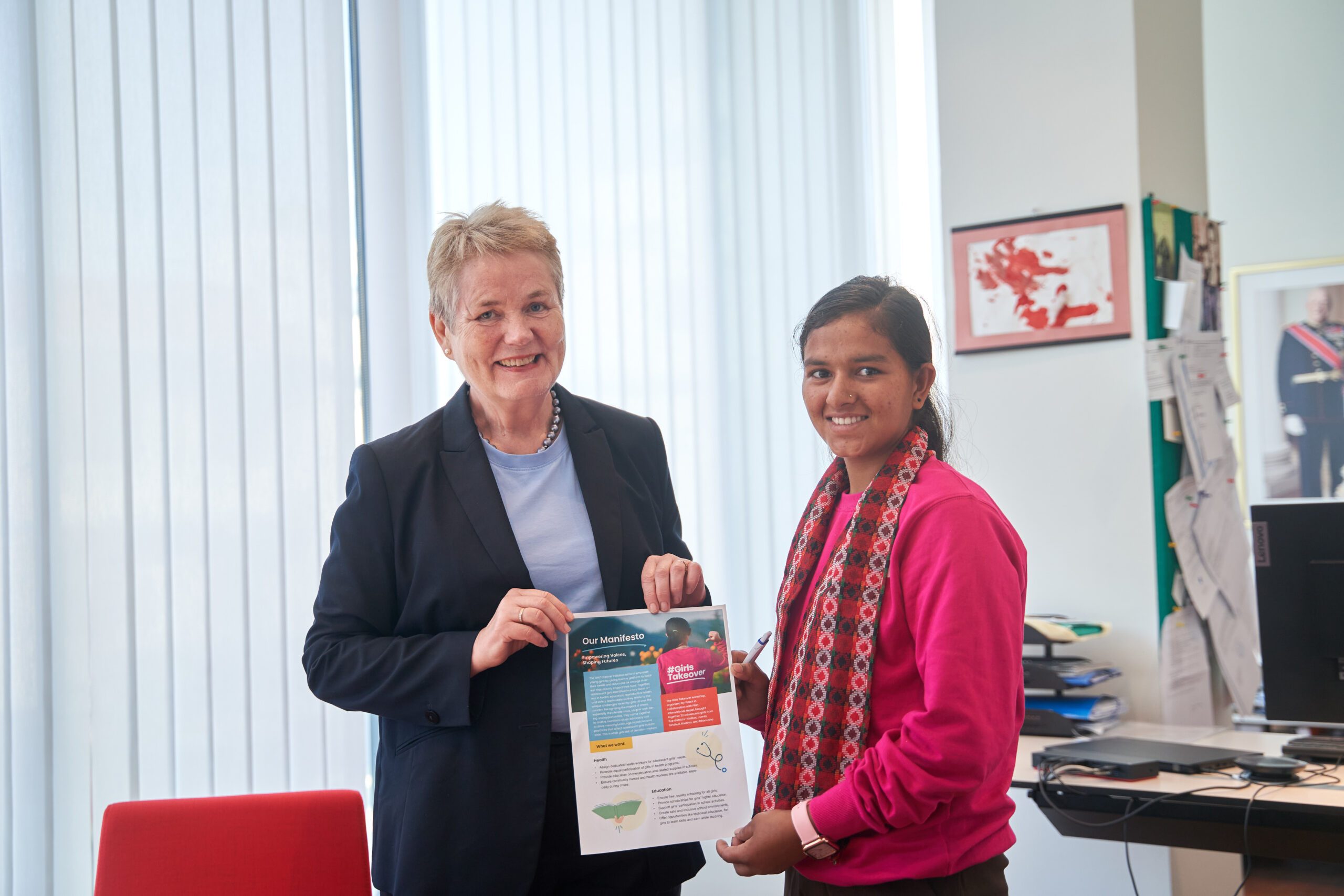 Norwegian ambassador wearing black coat on left and Lalita on right holding Girls' Manifesto. 