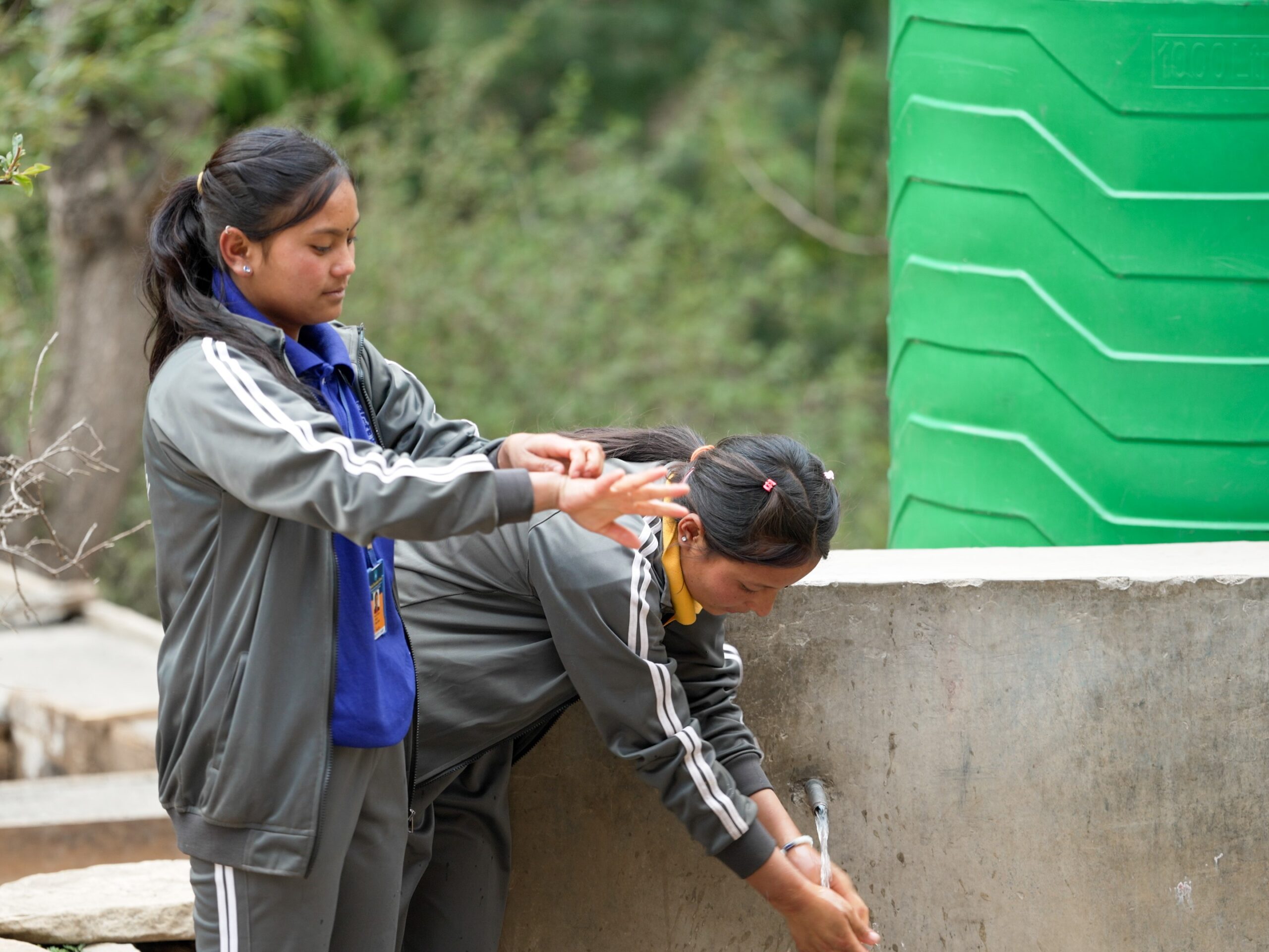 Two girls in their school uniforms washing their hands. 