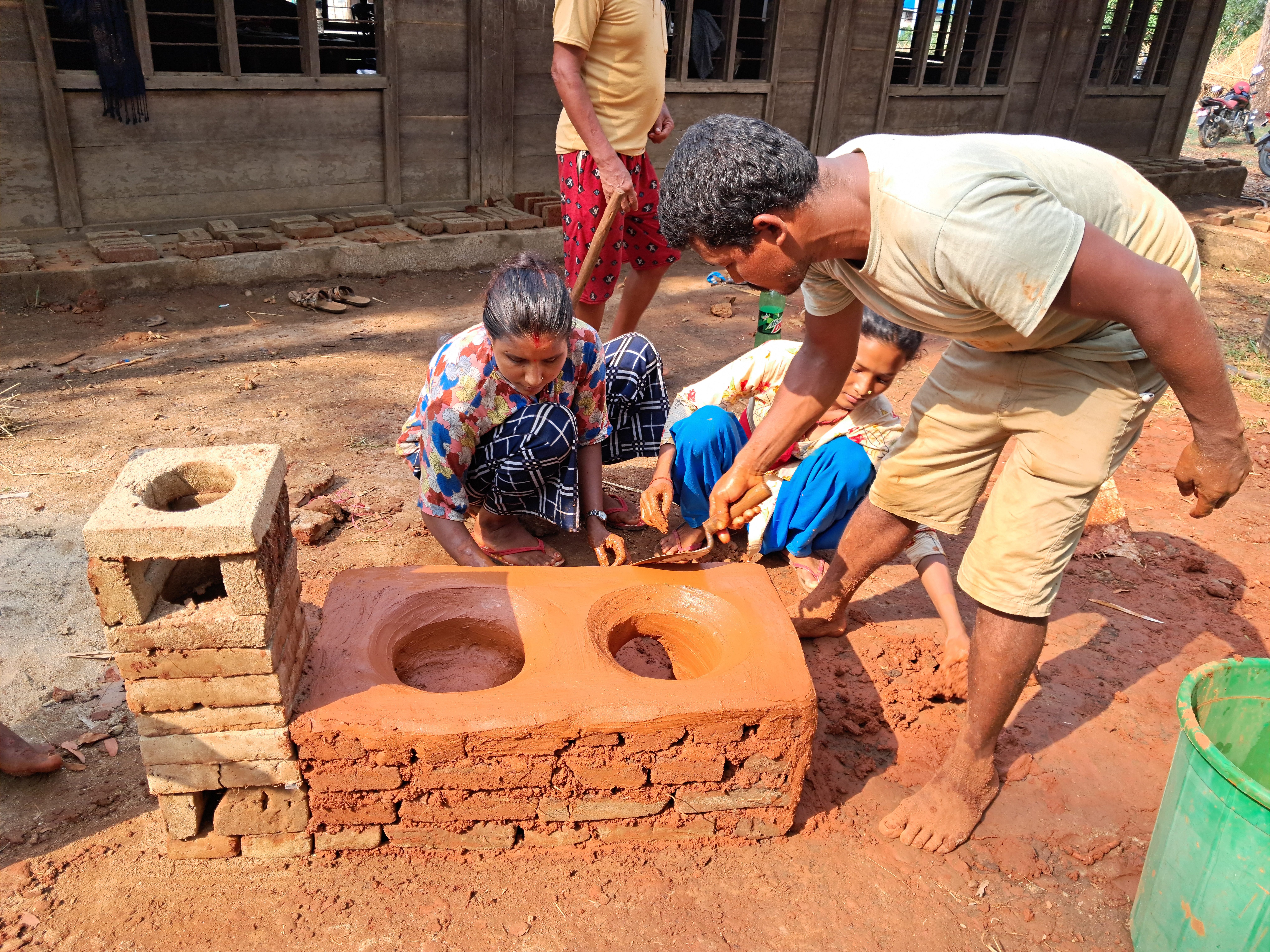 Two women and a man using clay and mud to make improved cooking stoves.