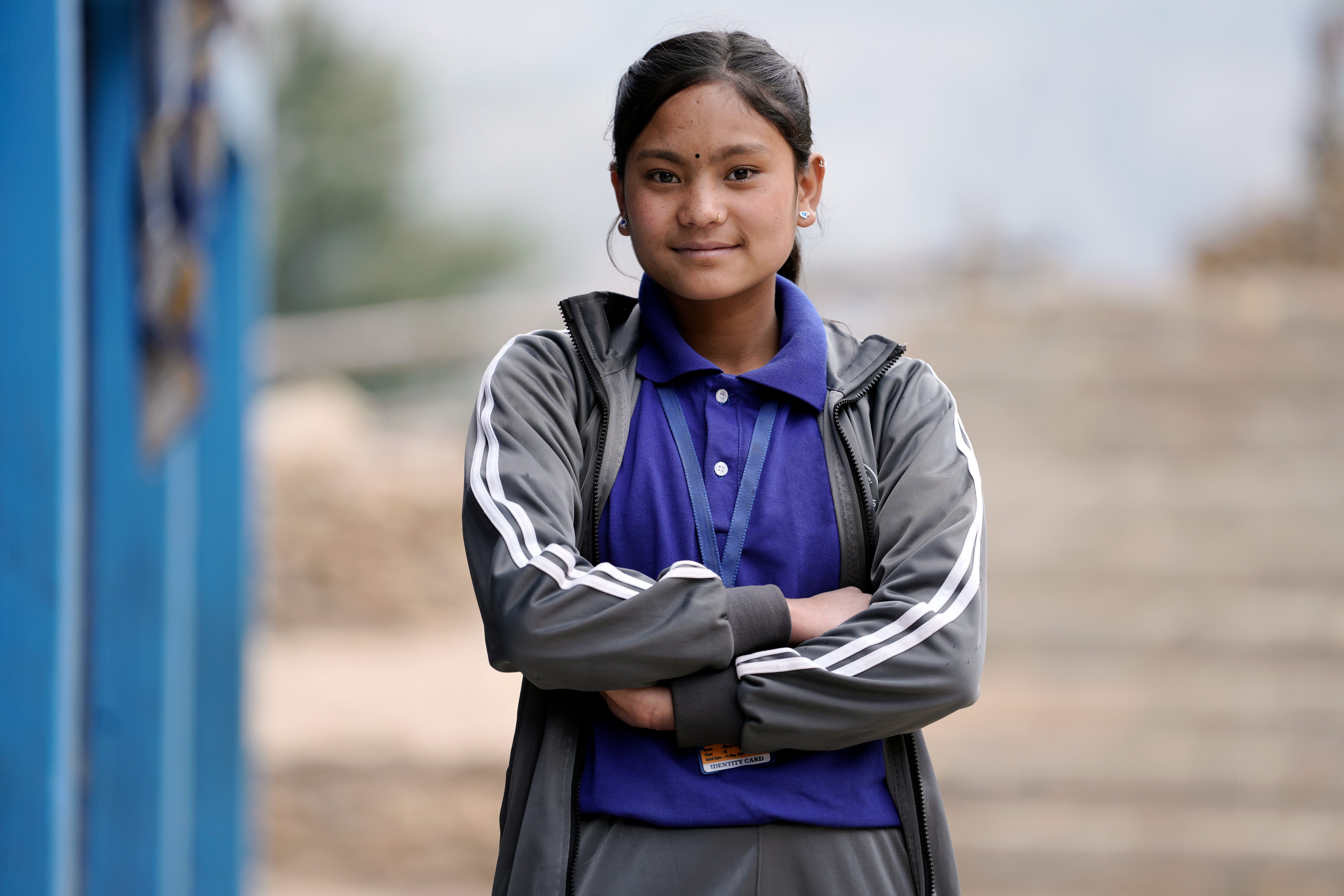 A young female student in a school uniform stands with her arms crossed.