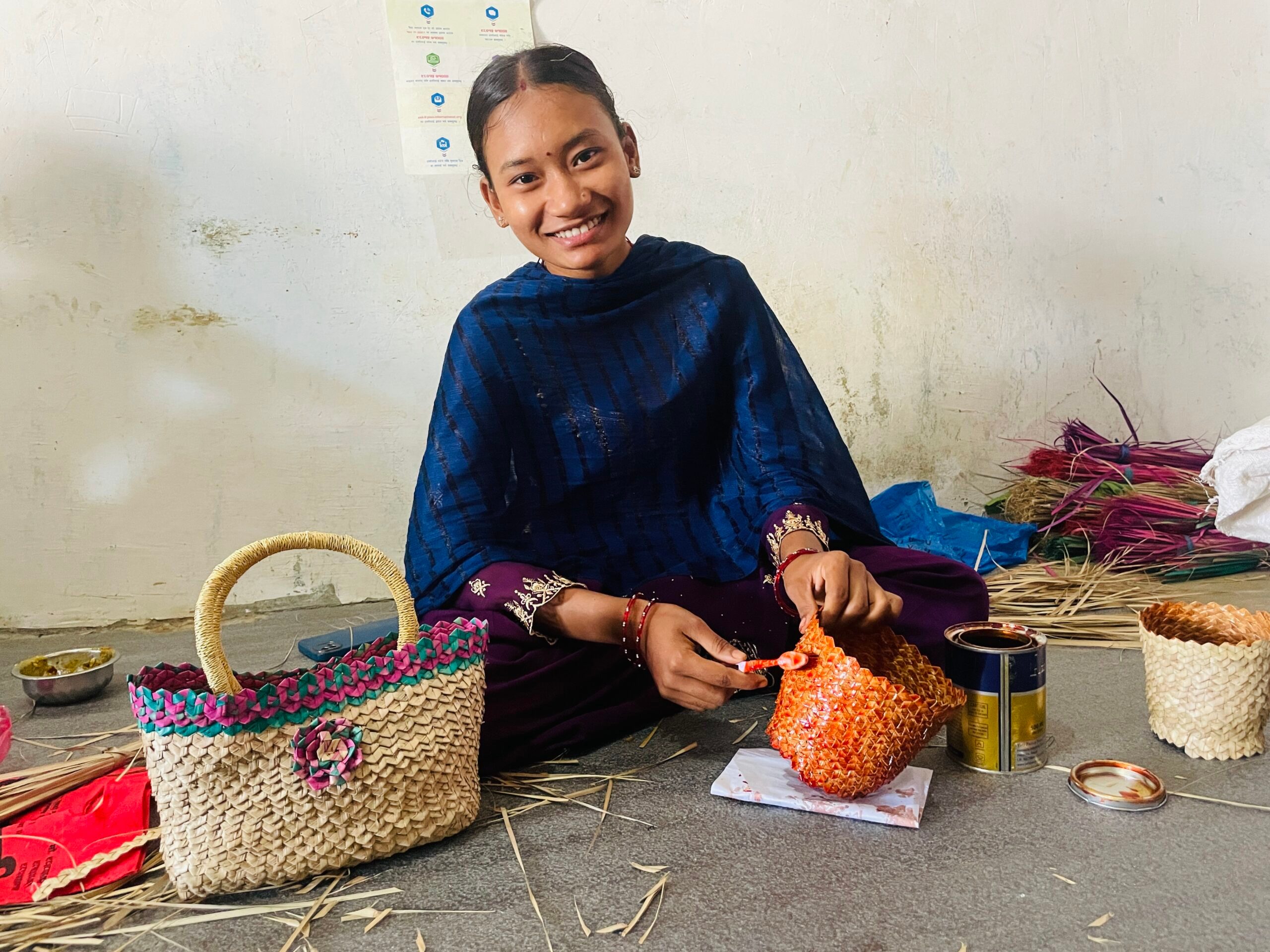 A young woman is wearing a blue shawl, holding a brush to paint the handicraft she is making.