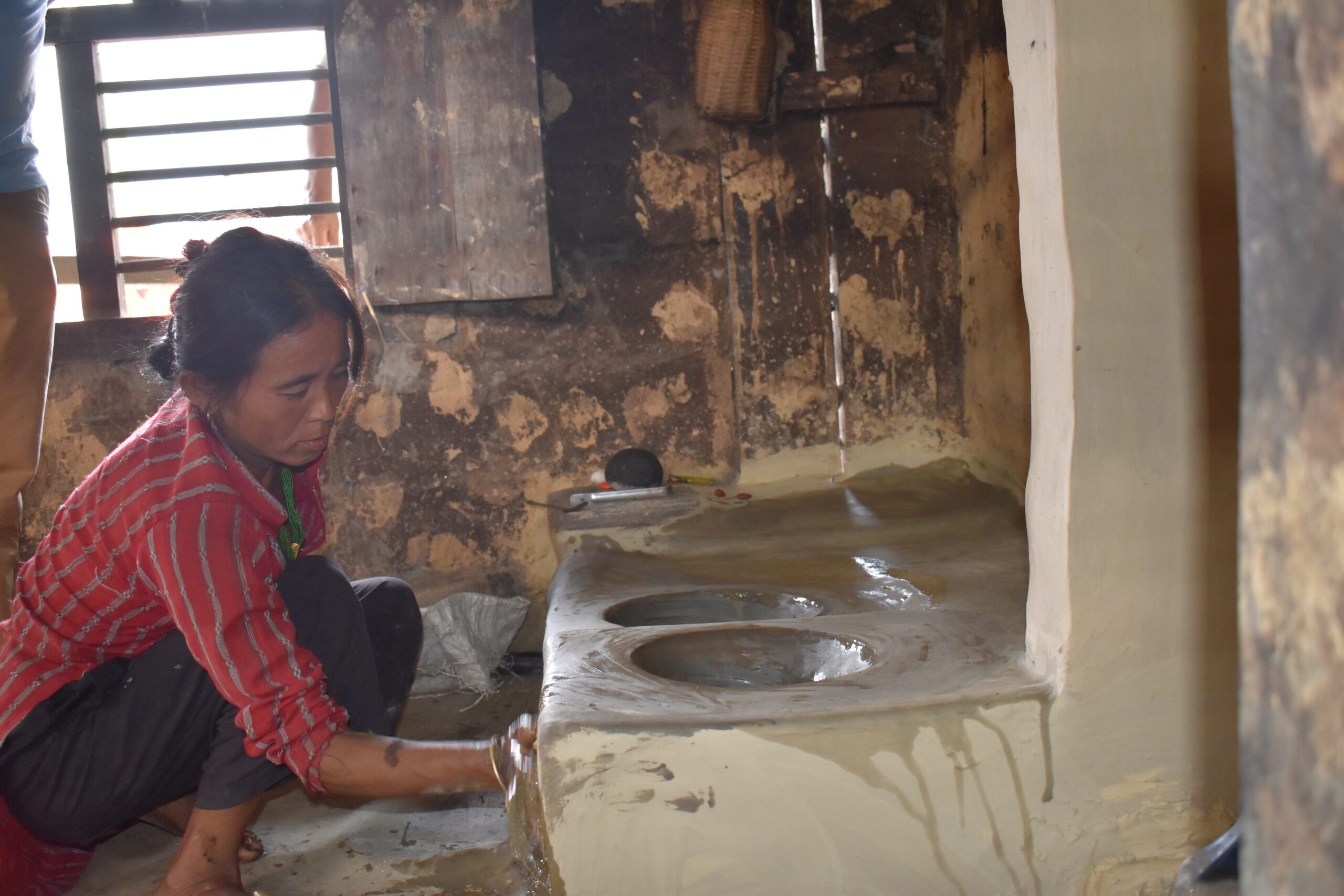 A middle age women sitting in front of newly built Improved Cooking Stoves and cleaning it.