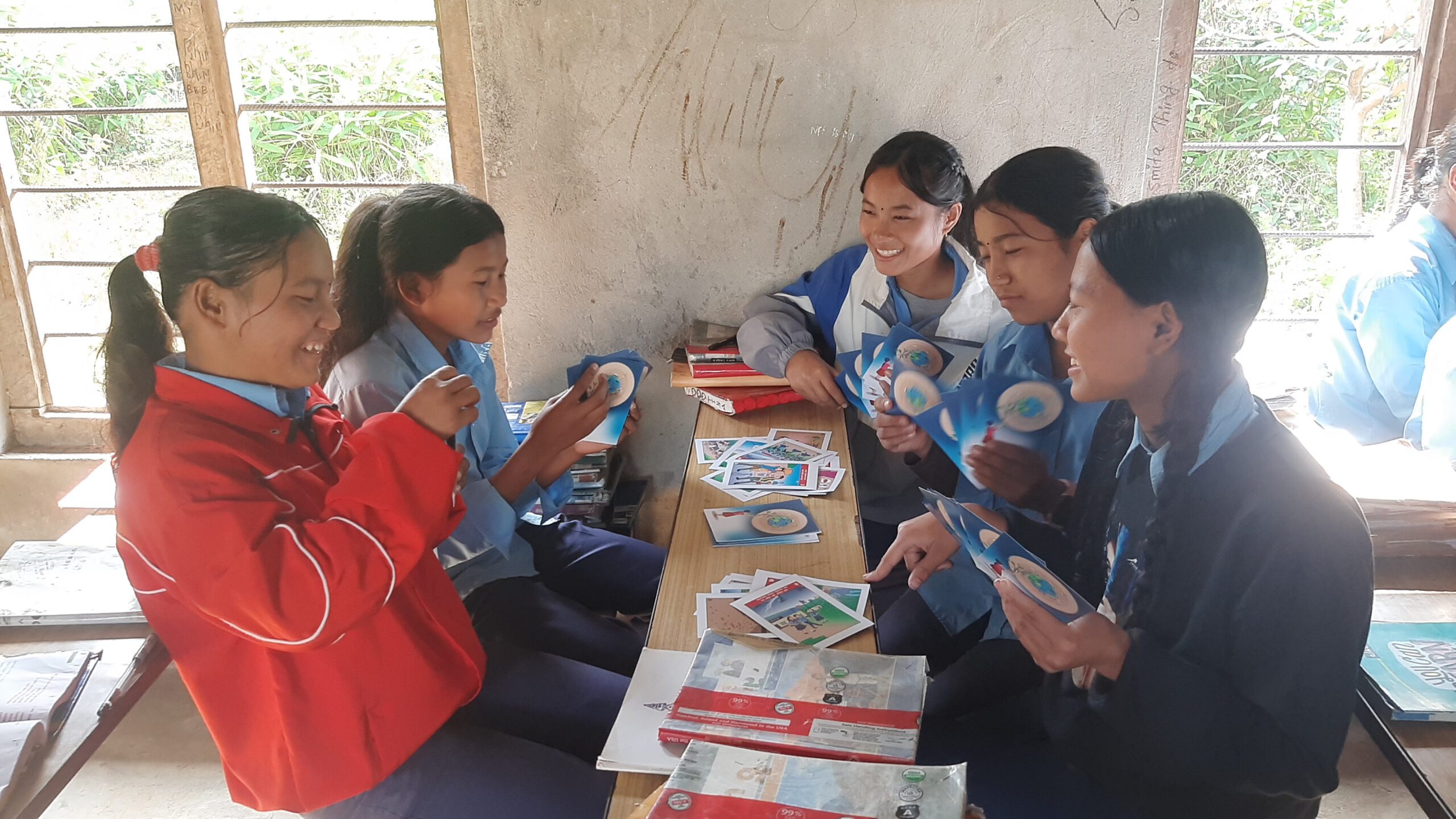 A group of female students (5) playing cards related to disaster risk reduction in their classrooms.