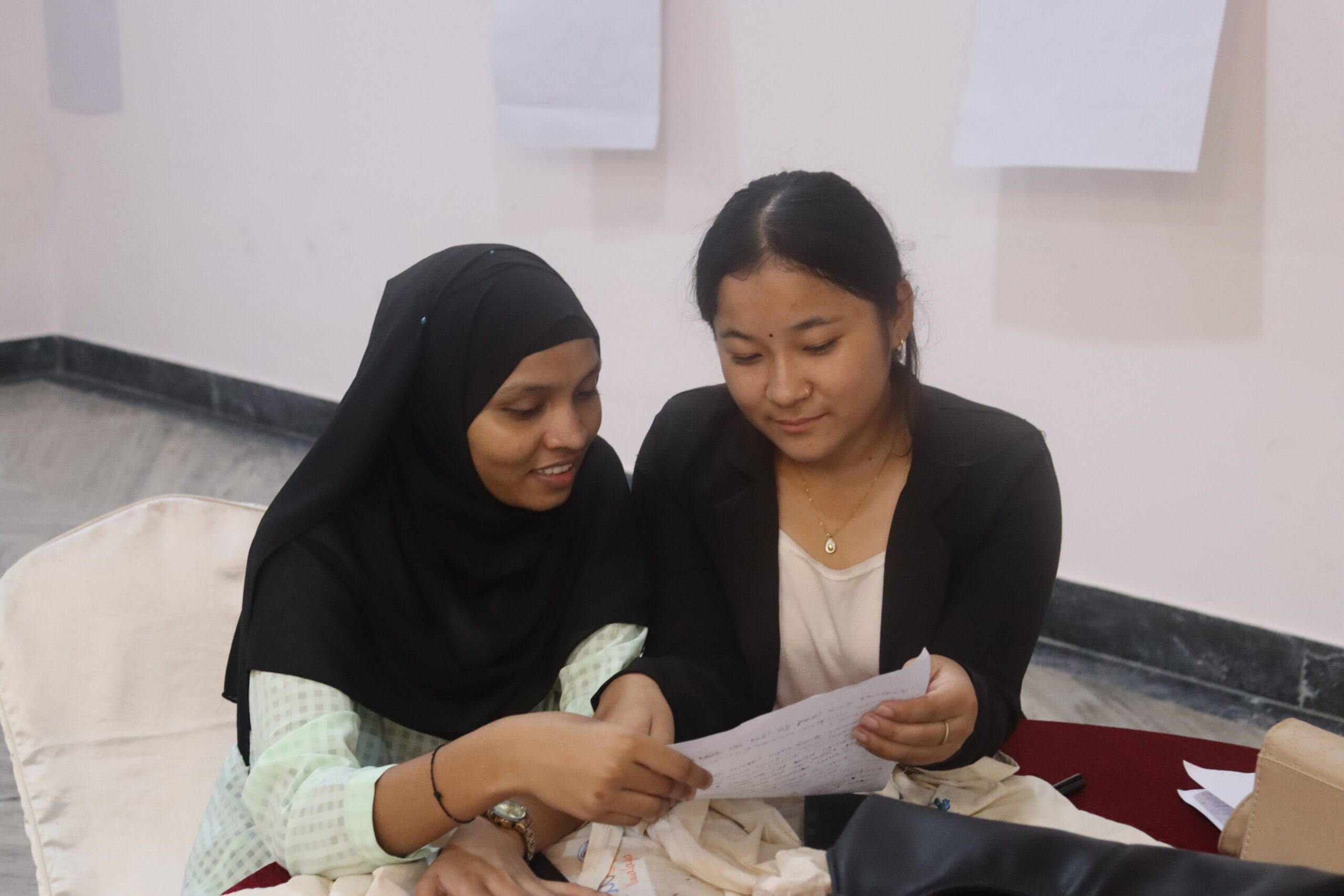 Two young women sitting together and holding a paper