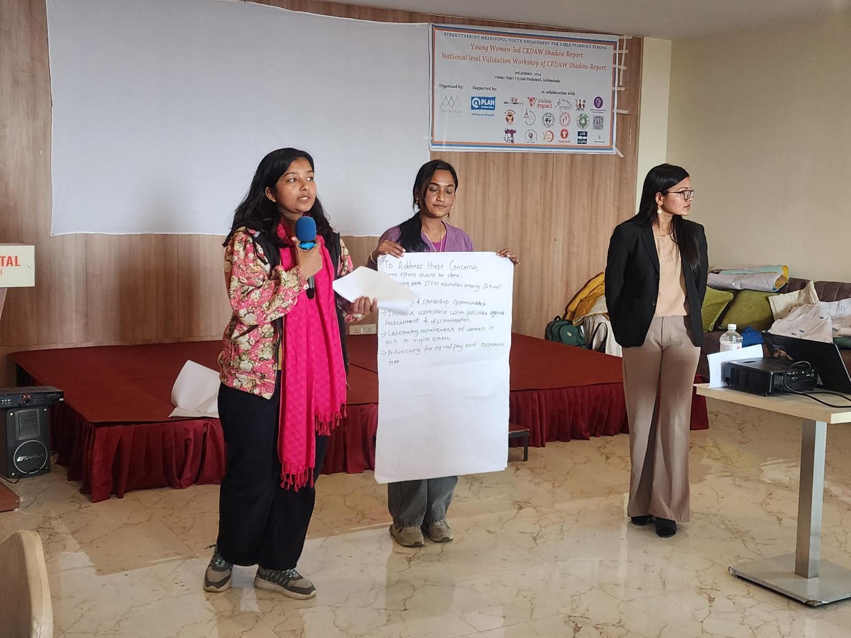 Three young women standing. Two women are holding a chart paper and presenting their work