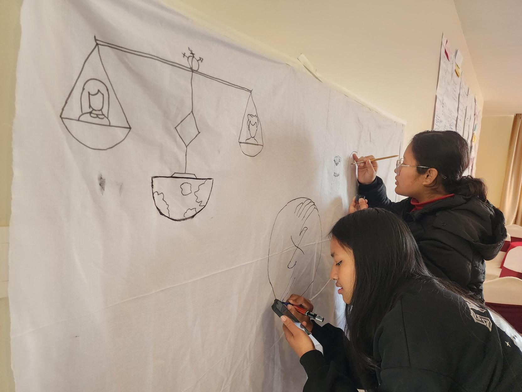 Two young girls holding brush to paint in a white cloth.