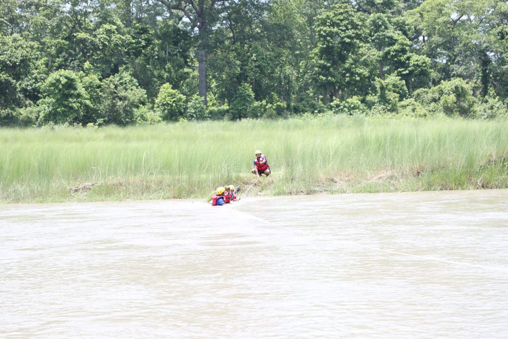 Three people wearing red life jackets using rope and rescuing people during flood preparedness drill.
