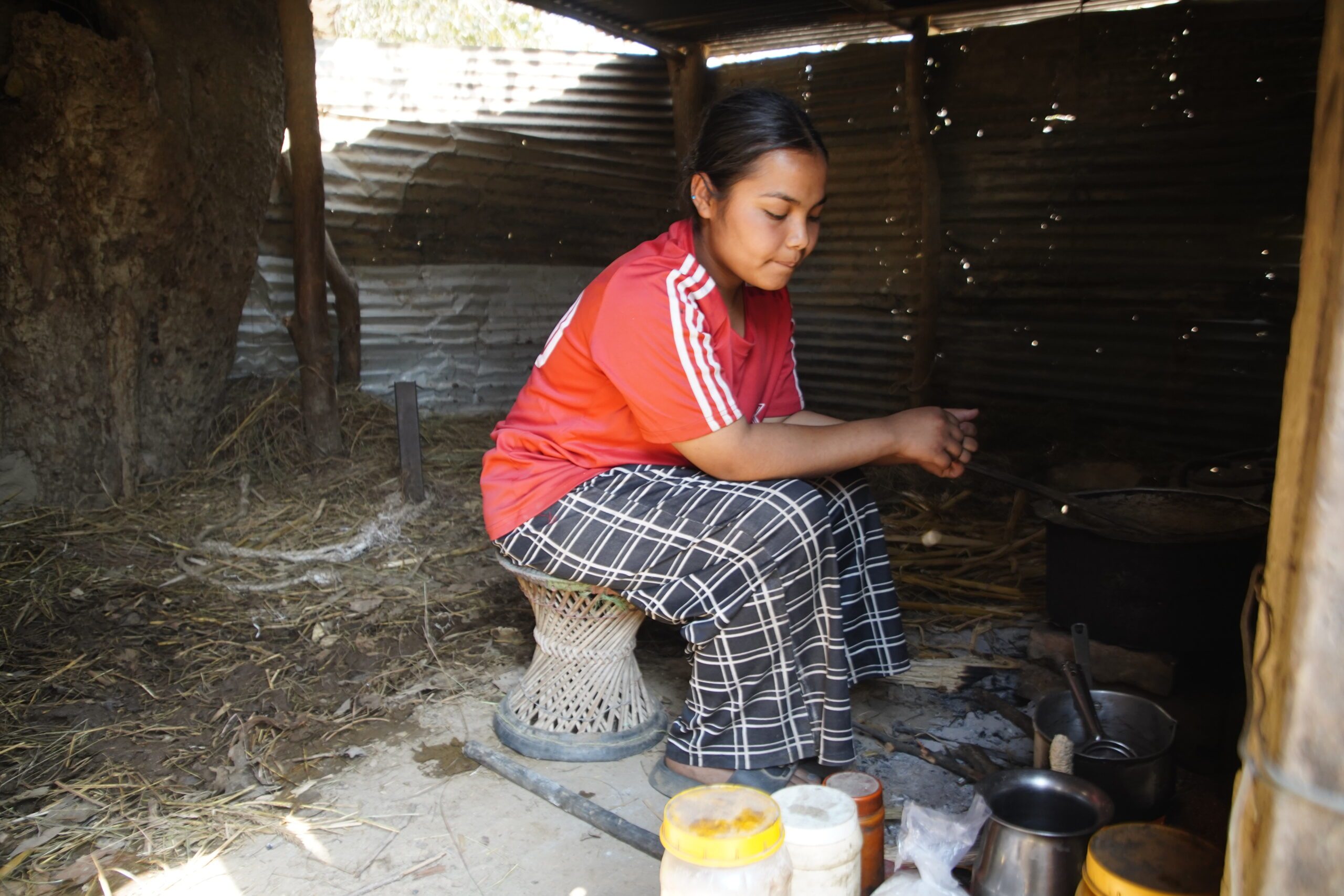 A girl wearing red t-shirt is preparing tea in a kitchen shifted outside after flood.