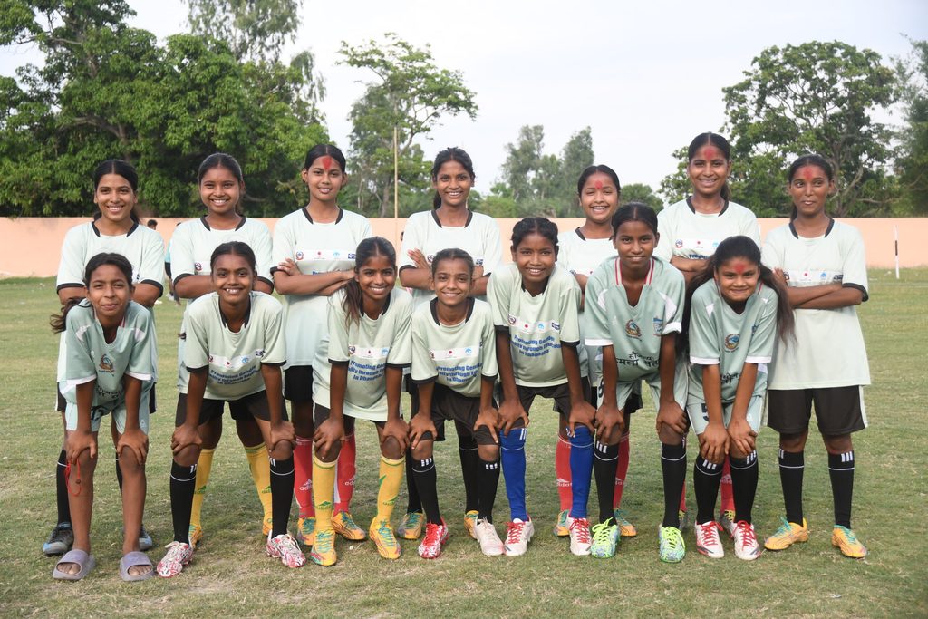 A group of girl's football team in Madhesh wearing jersey and posing for a photo in football ground.