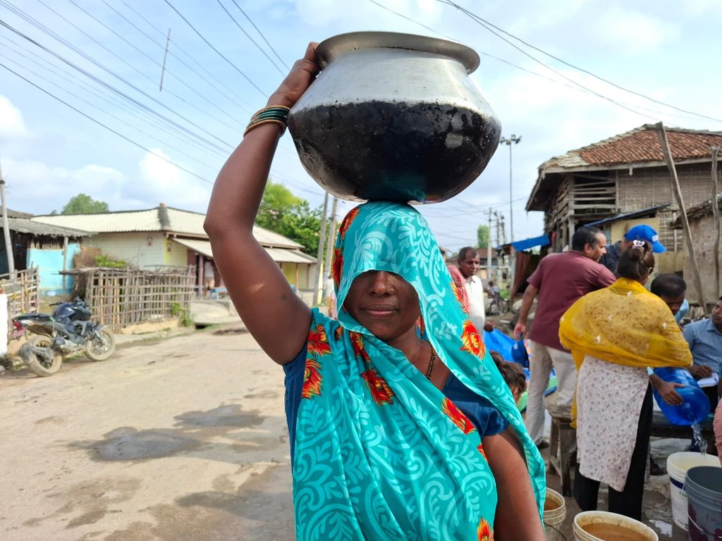 A woman wearing sari carrying water vessel on her head and her face covered with the sari.