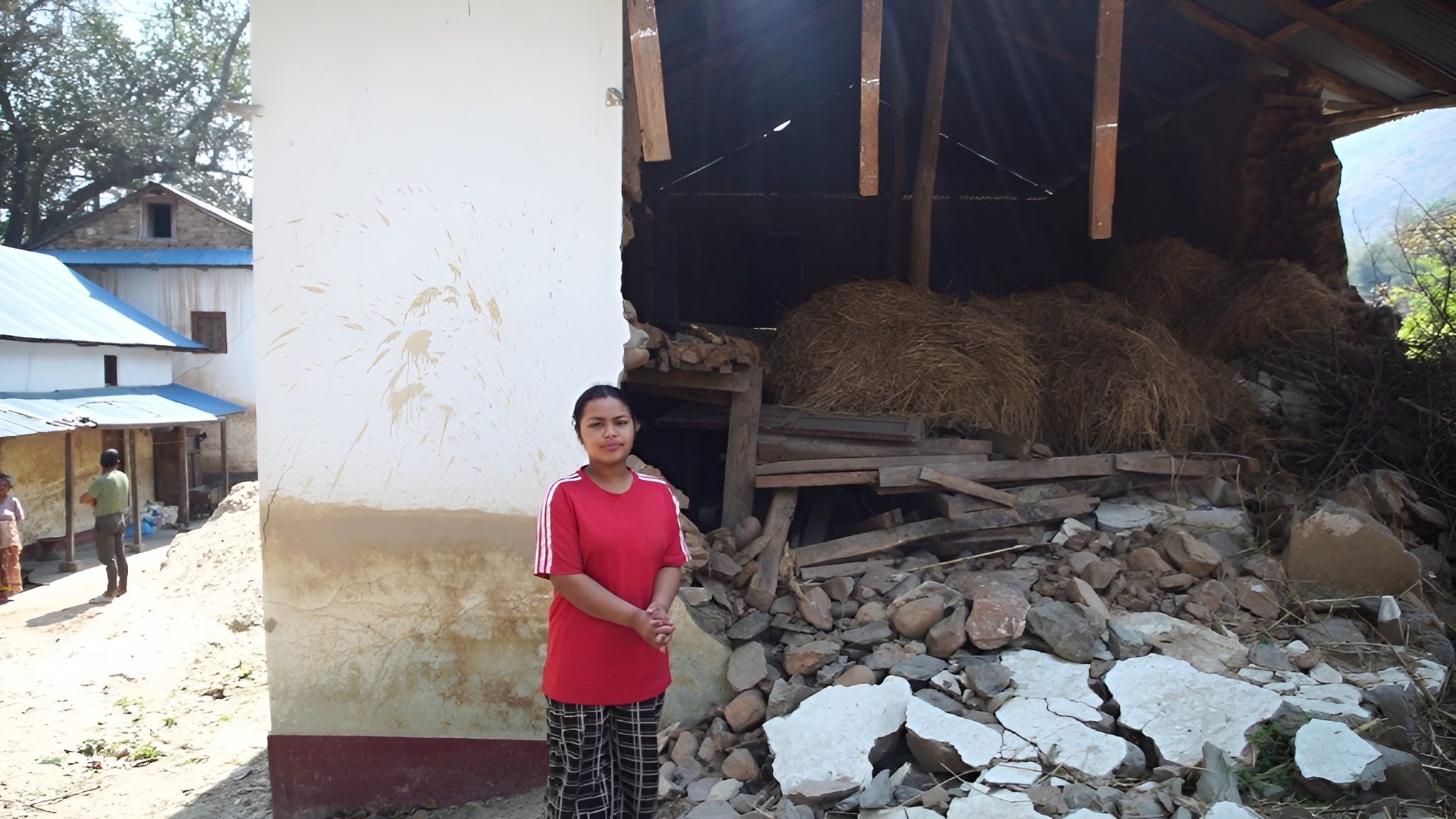 A girl wearing red t-shirt standing in front of her house affected by flood. 
