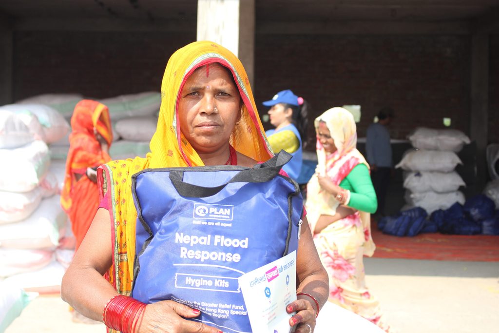 A woman holding blue bag with Plan logo and receiving hygiene kits during flood response in Saptari.