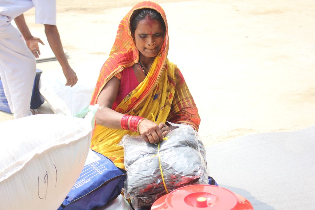 A woman in a sari sits down as she ties up relief materials in Saptari district.