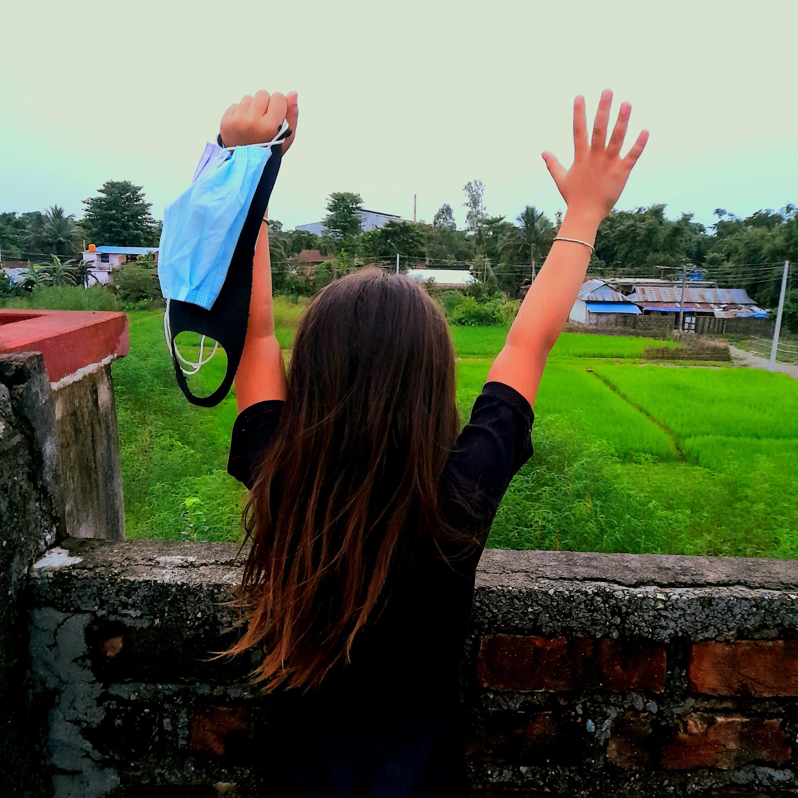 A girl looking at the field, both hands up, in left hand holding masks