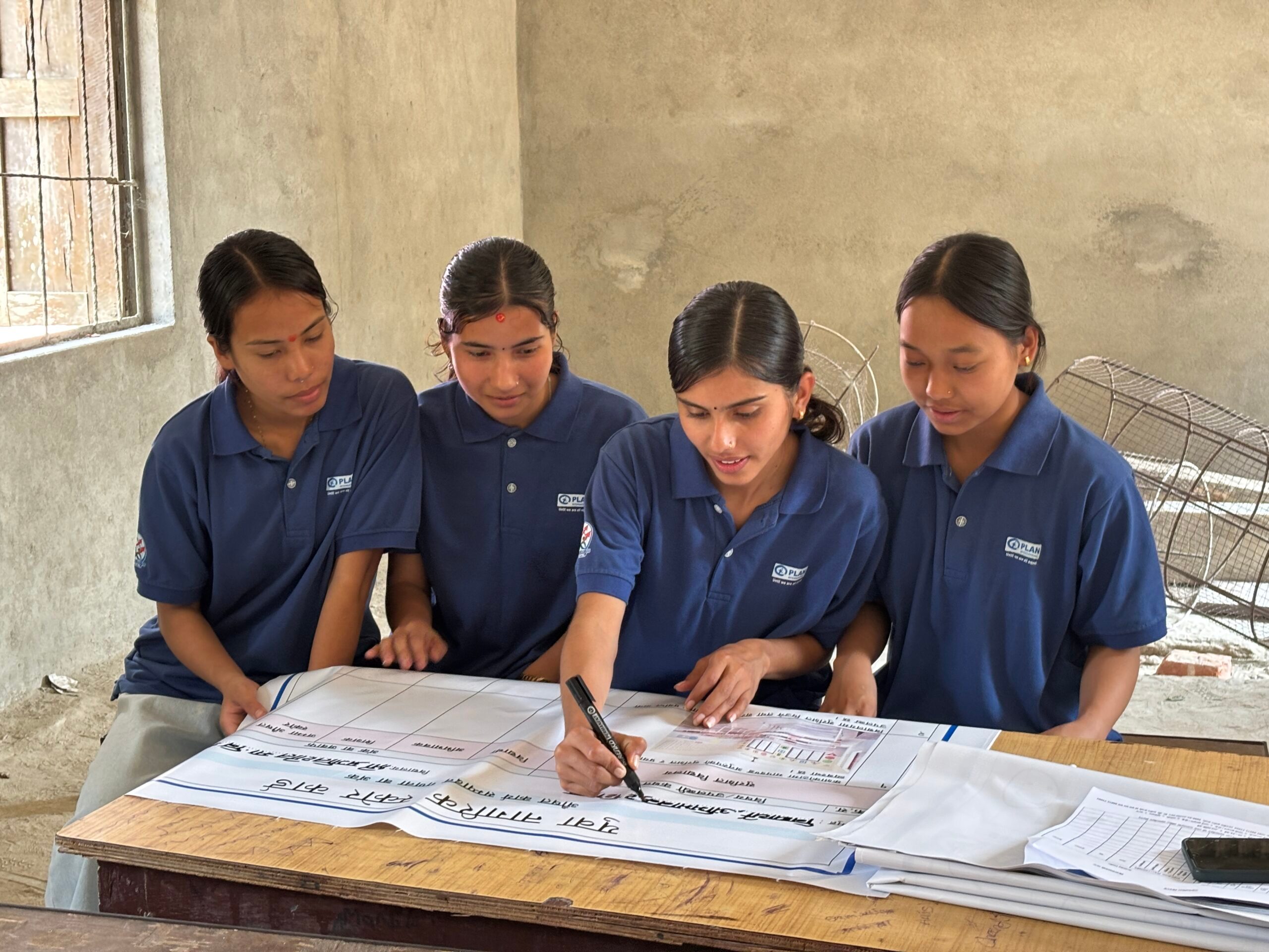 Four young girls sitting on the school tables and ticking the youth citizen score card.