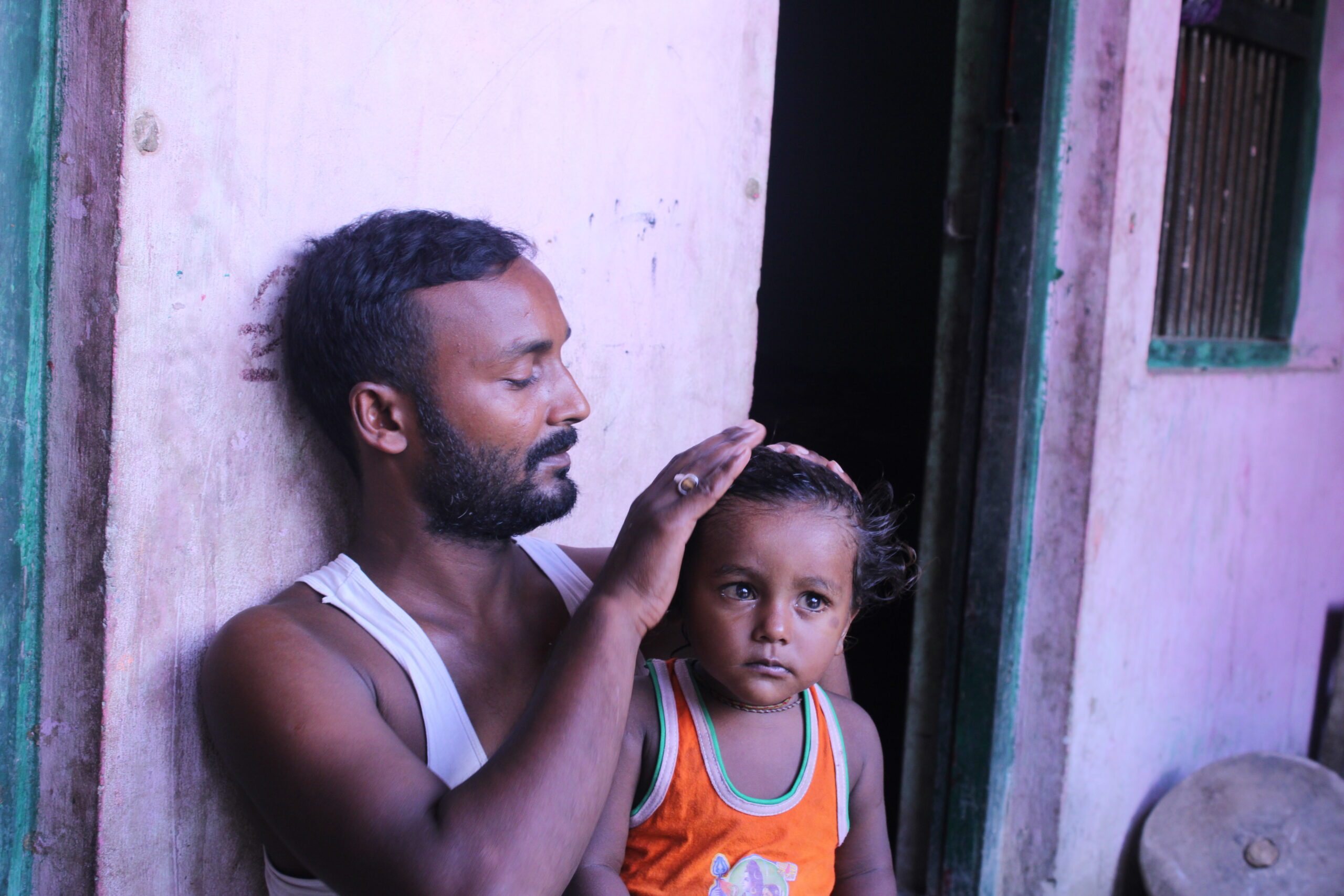 A father and a child sitting outside their home. Father combing his hair.