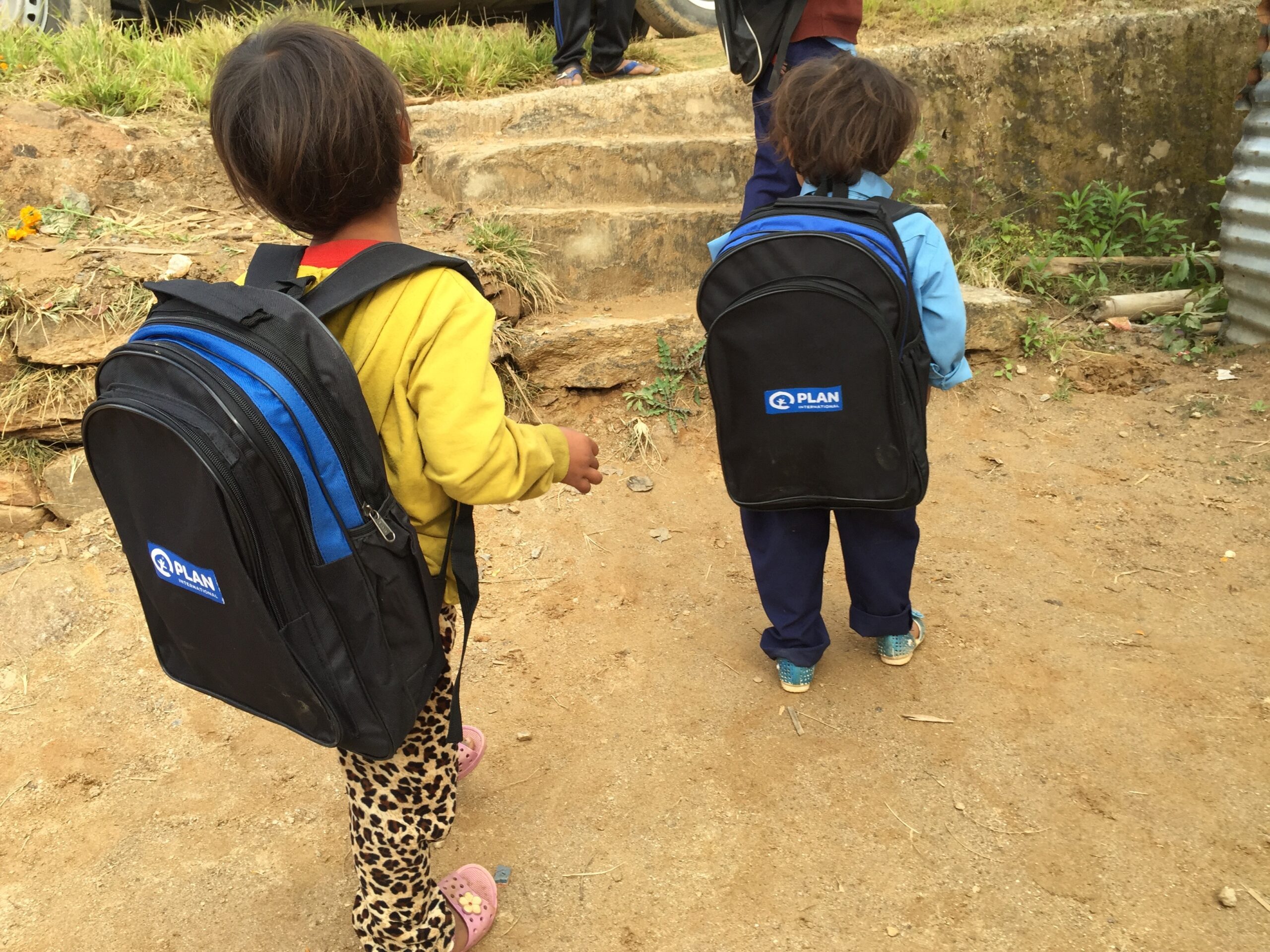Two children carrying school bag with Plan's logo and going to transitional learning centre in Sindhupalchowk after 2015 earthquake.