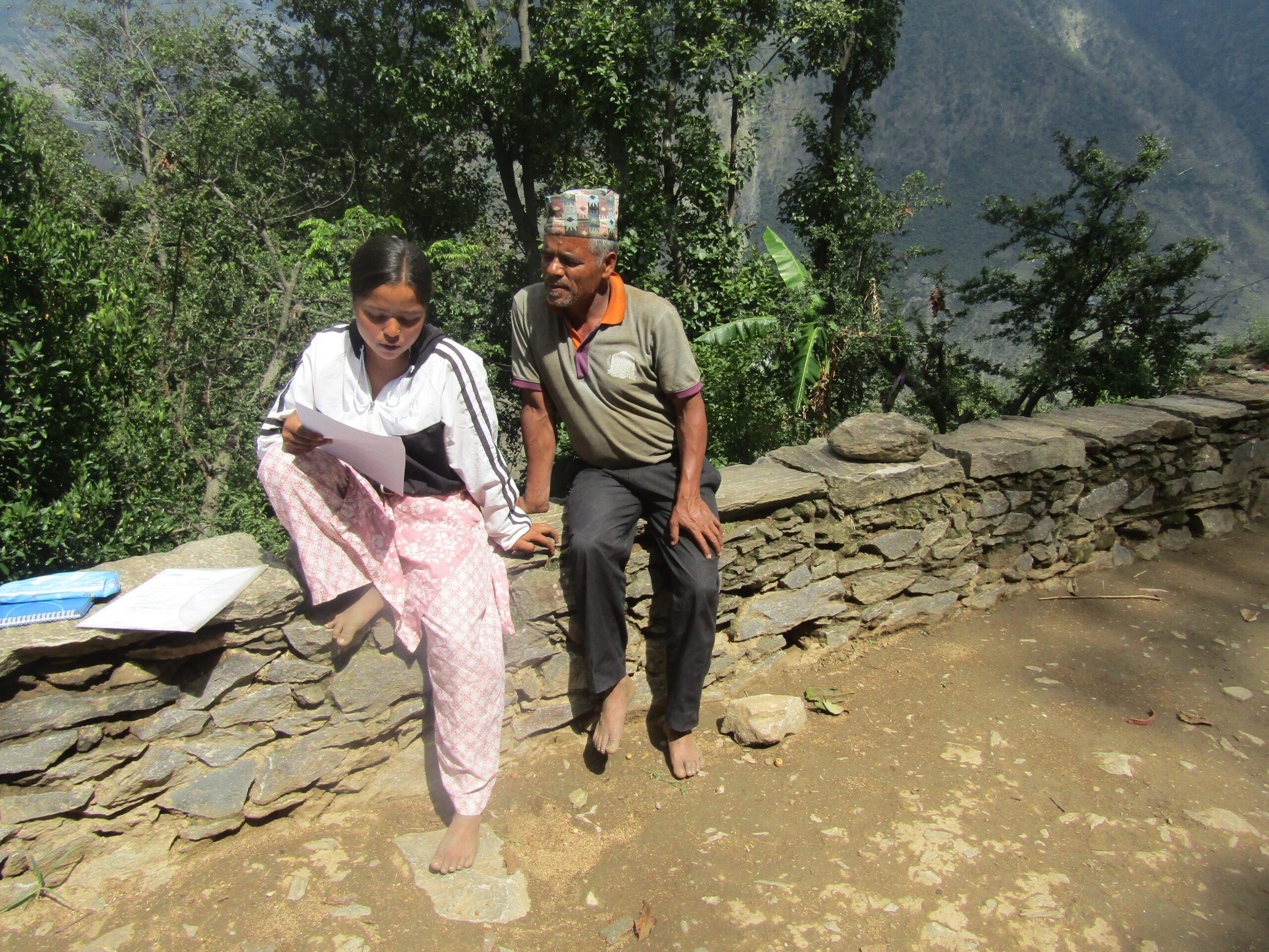 A father and daughter in their garden. Father watching her daughter read a document. 