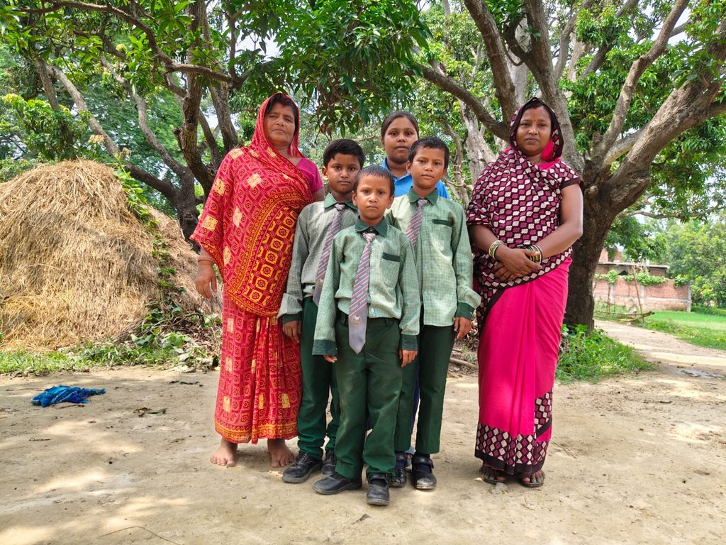Four children (3 boys and 1 girl) in school uniform standing in between their grand mother and mother.