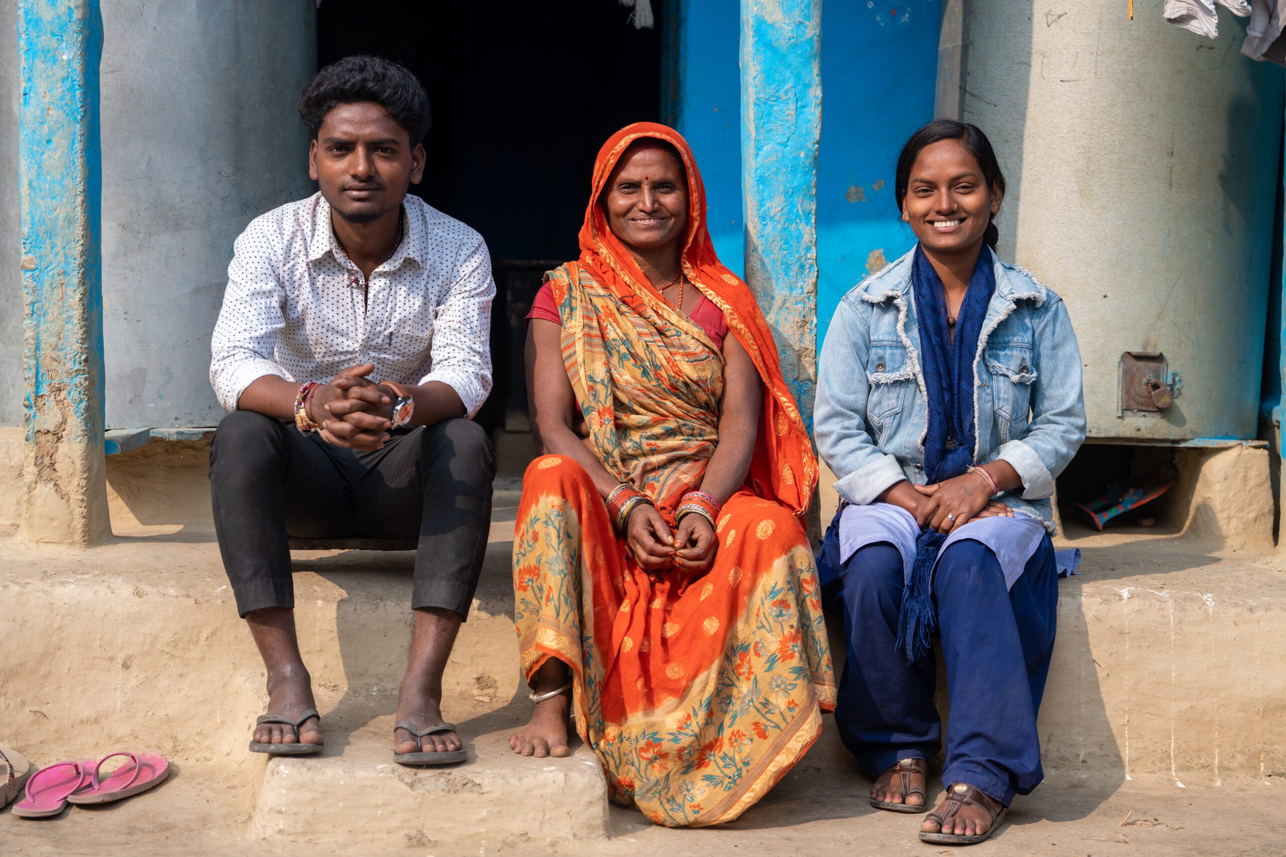 Ashiya (right) sitting in front of her house with her mother (middle) wearing sari and brother (left)