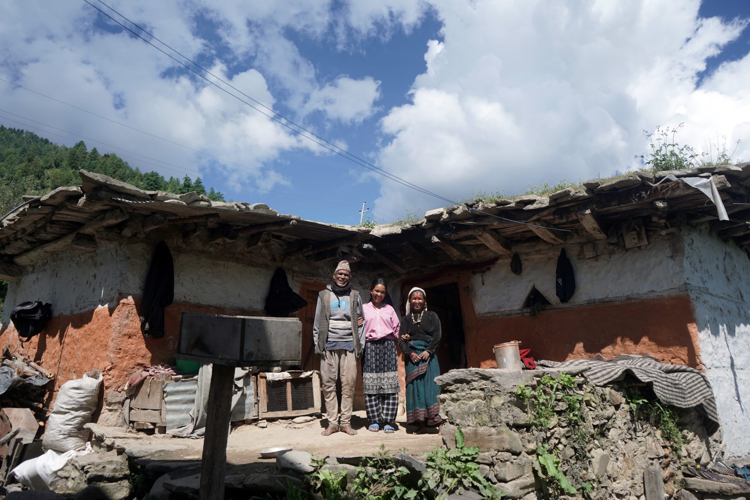 Shivalaxmi standing with her parent in front of her house.