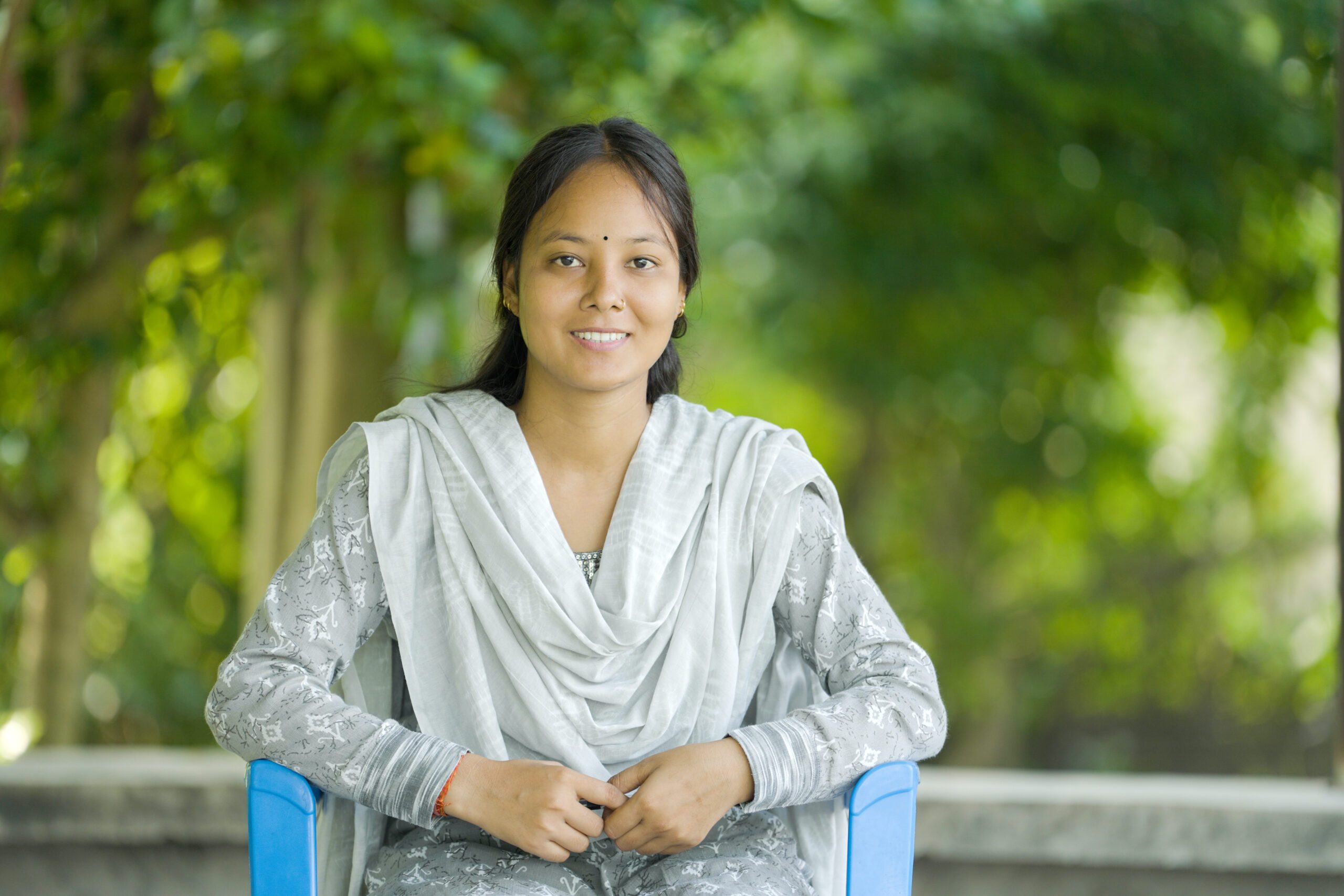 A young women sitting on a chair with background of trees. 