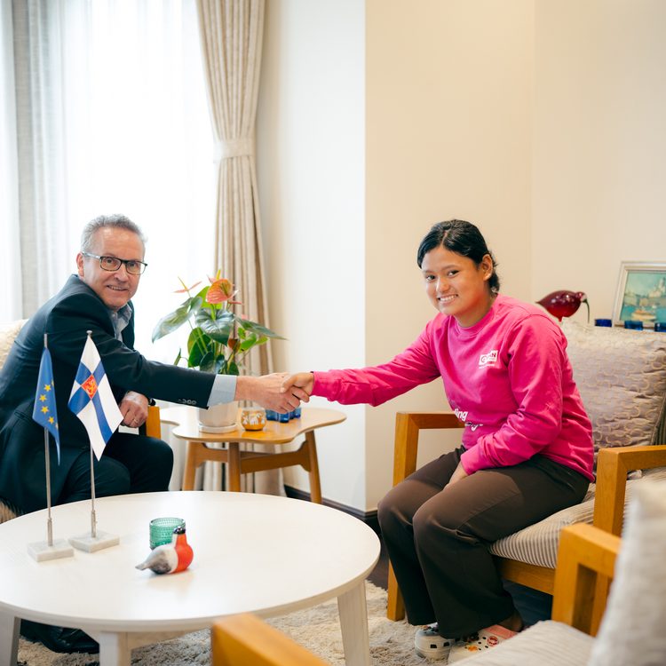 A man in black suit on left and girl in pink in right shaking their hands.
