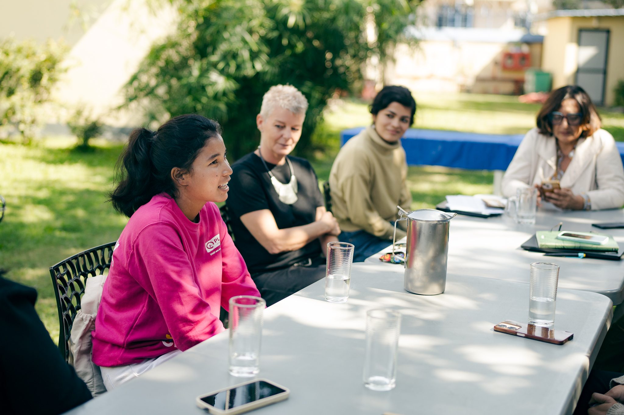 Aruna sitting in a chair with other three women beside her and talking.