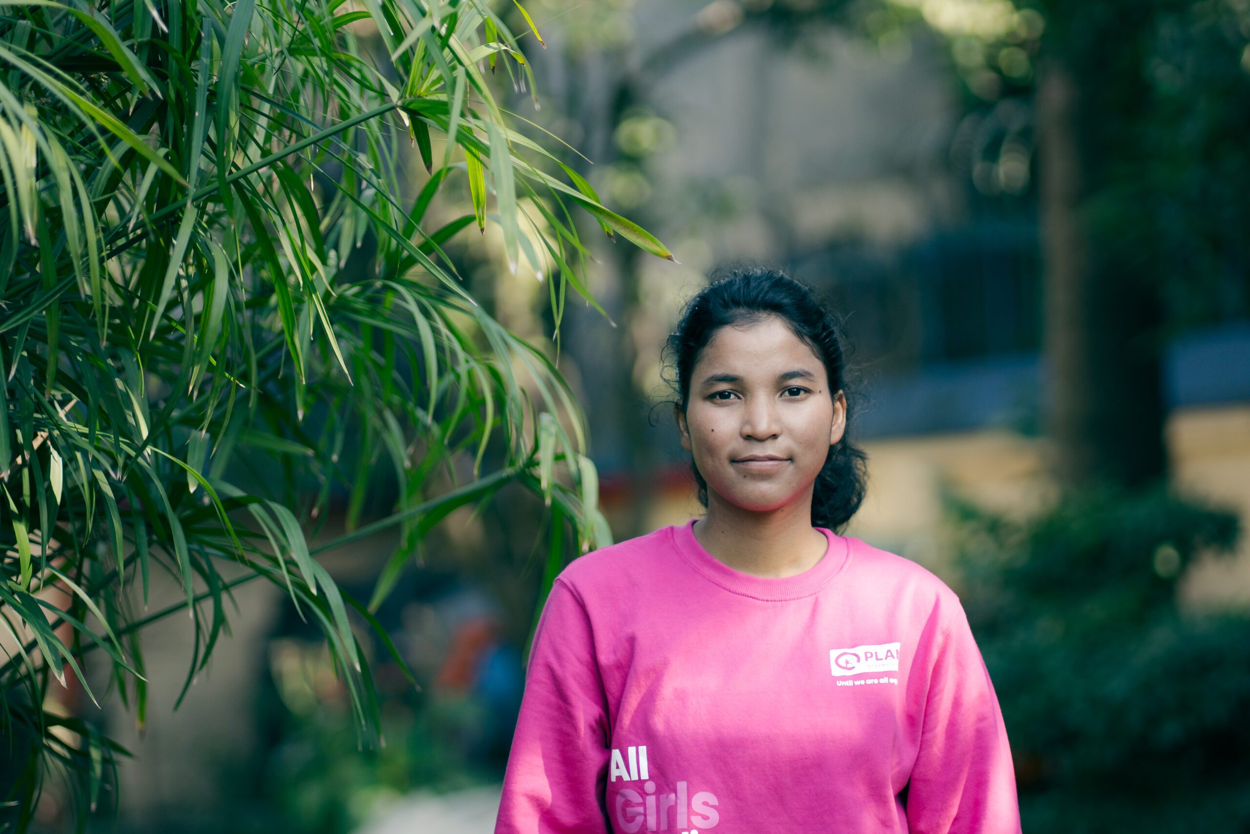A young girls wearing pink sweat tshirt with Plan's logo and smiling at camera. 