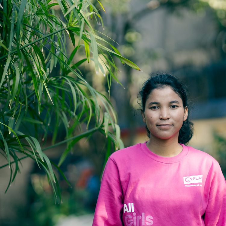 A young girls wearing pink sweat tshirt with Plan's logo and smiling at camera.