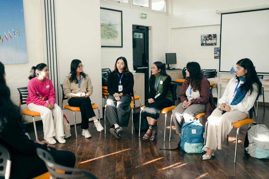A group of young girls sitting on a chair and attending a meeting.