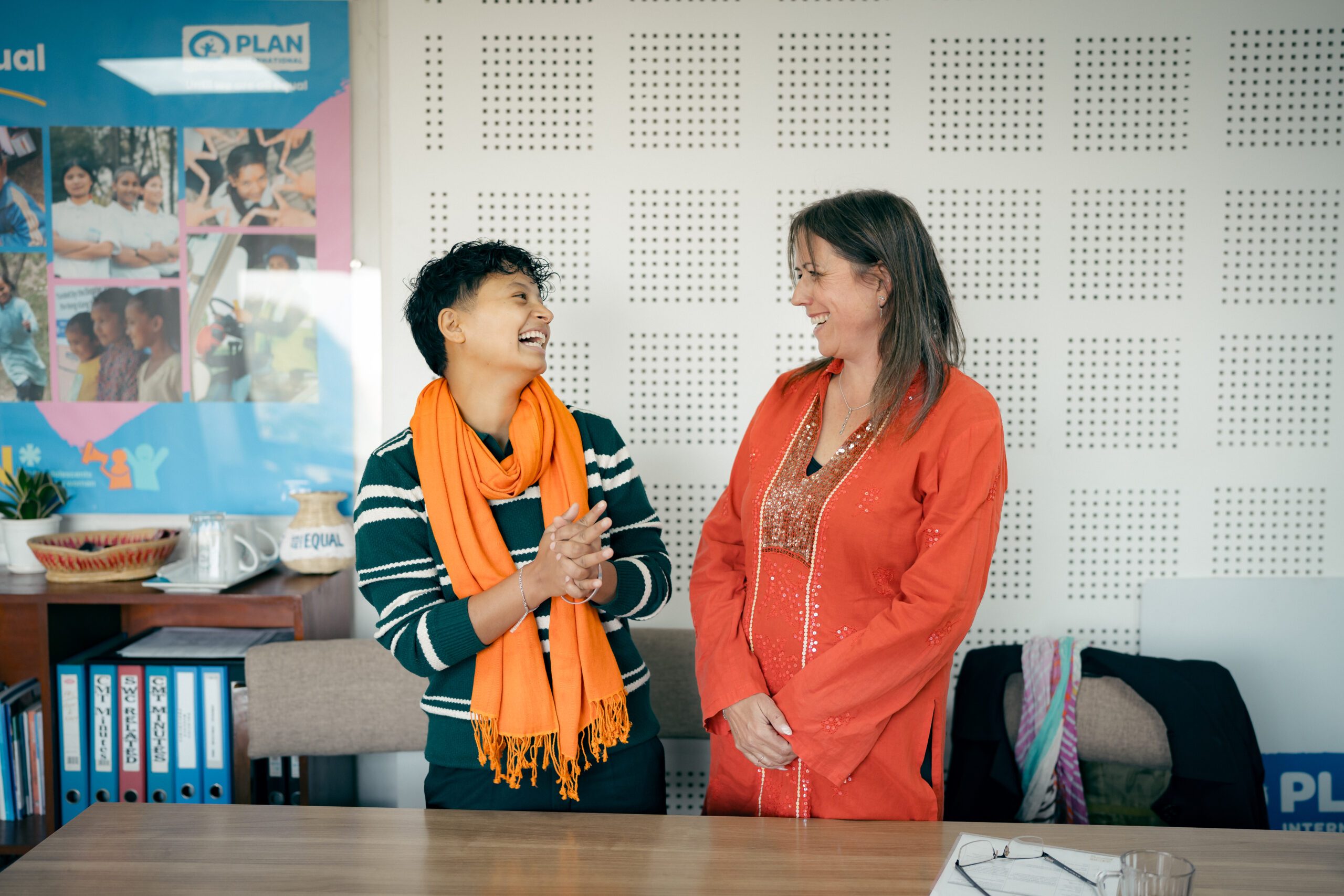 Anu, a trans man on left wearing orange scarf and Pippa, Development Director at FCDO on right standing and having jolly moment.