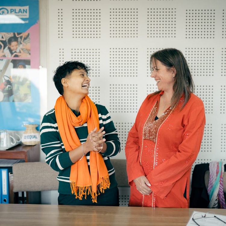 Anu, a trans man on left wearing orange scarf and Pippa, Development Director at FCDO on right standing and having jolly moment.