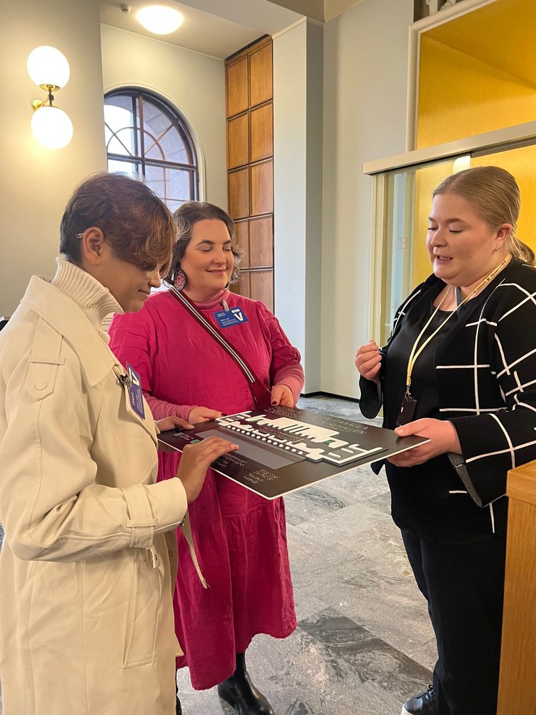 Smarika, wearing a white coat, touches the outline of the Finland Parliament House during a guided tour.