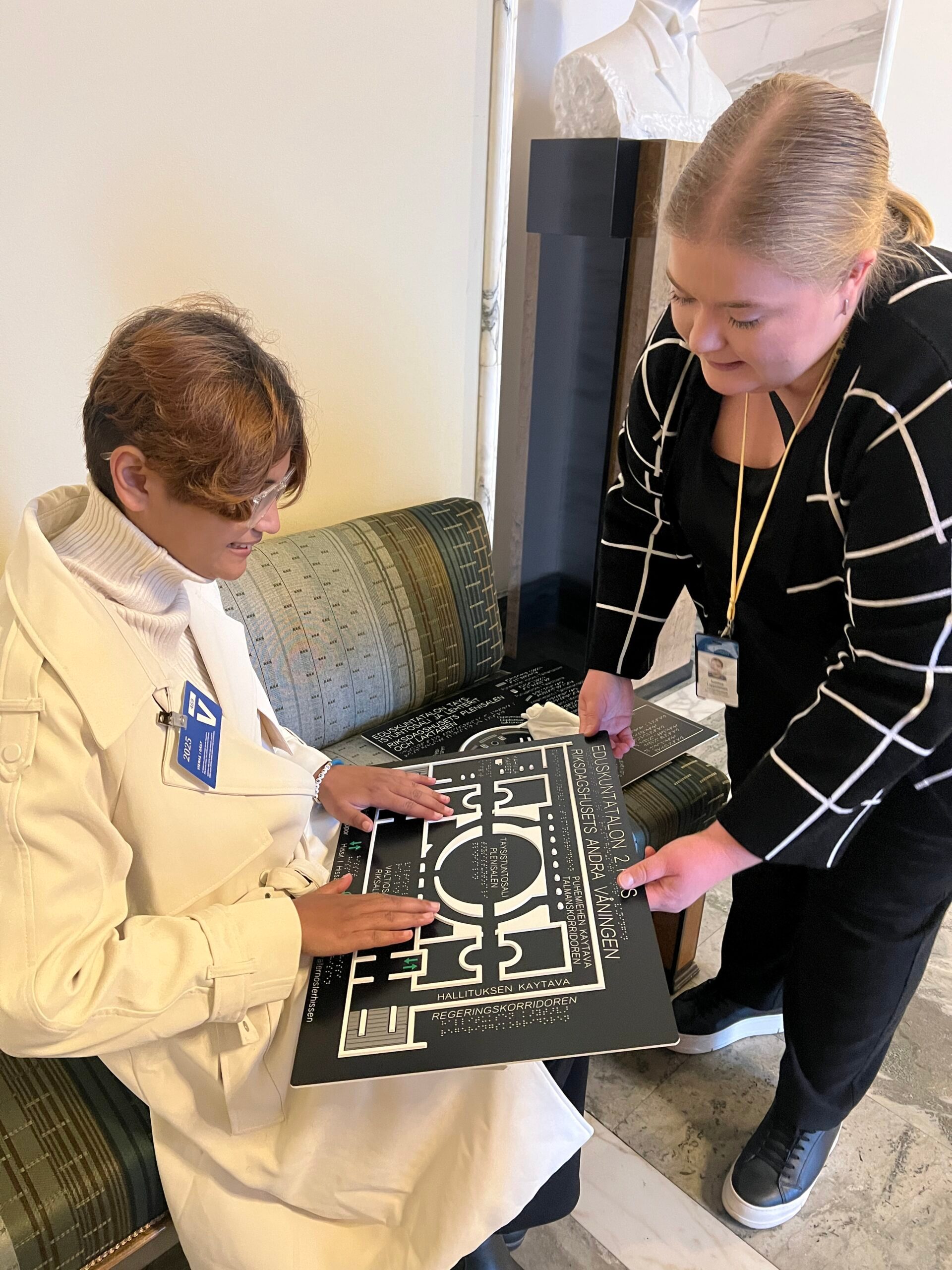 Smarika, wearing a white coat, touches the outline of the Finland Parliament House during a guided tour.