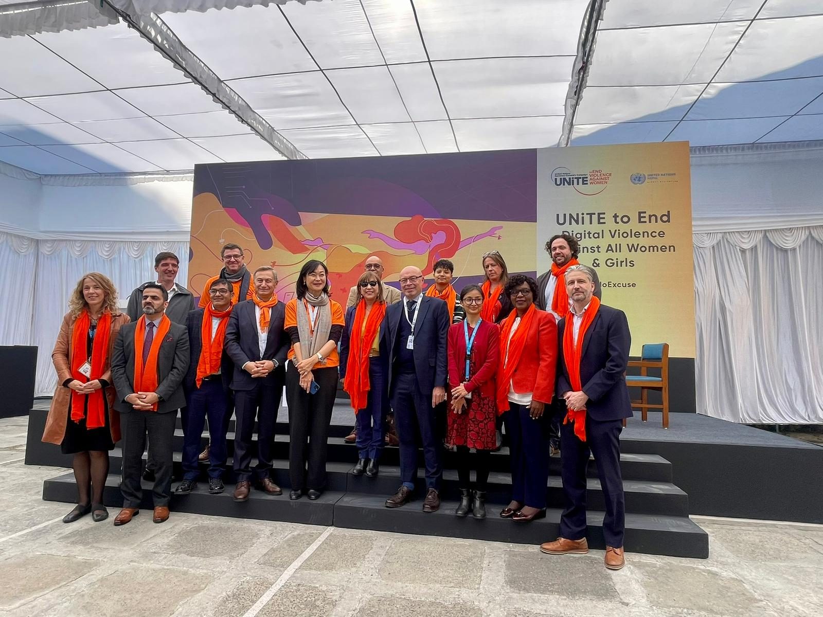 A group of people wearing orange, standing on a stage of 16 days of activism