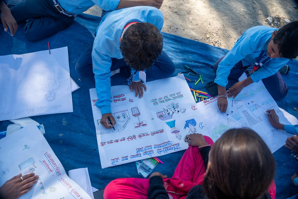 Students in school uniforms sitting on a blue carpet, drawing and colouring together.