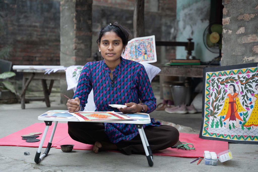 Ruhi, a young woman wearing blue dress sitting and holding brush and color to paint